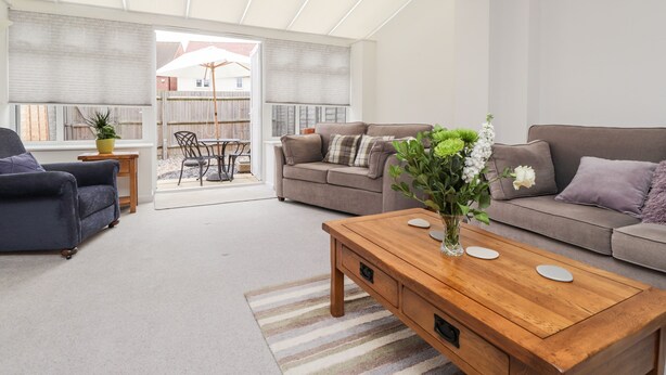 A modern living room with a sofa, a coffee table, and a dining area with a table and chairs. - 60 Galley Hill View (Bexhill-on-Sea)