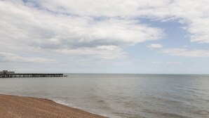 A beach with a wooden pier extending into calm waters under a partly cloudy sky. - 60 Galley Hill View (Bexhill-on-Sea)