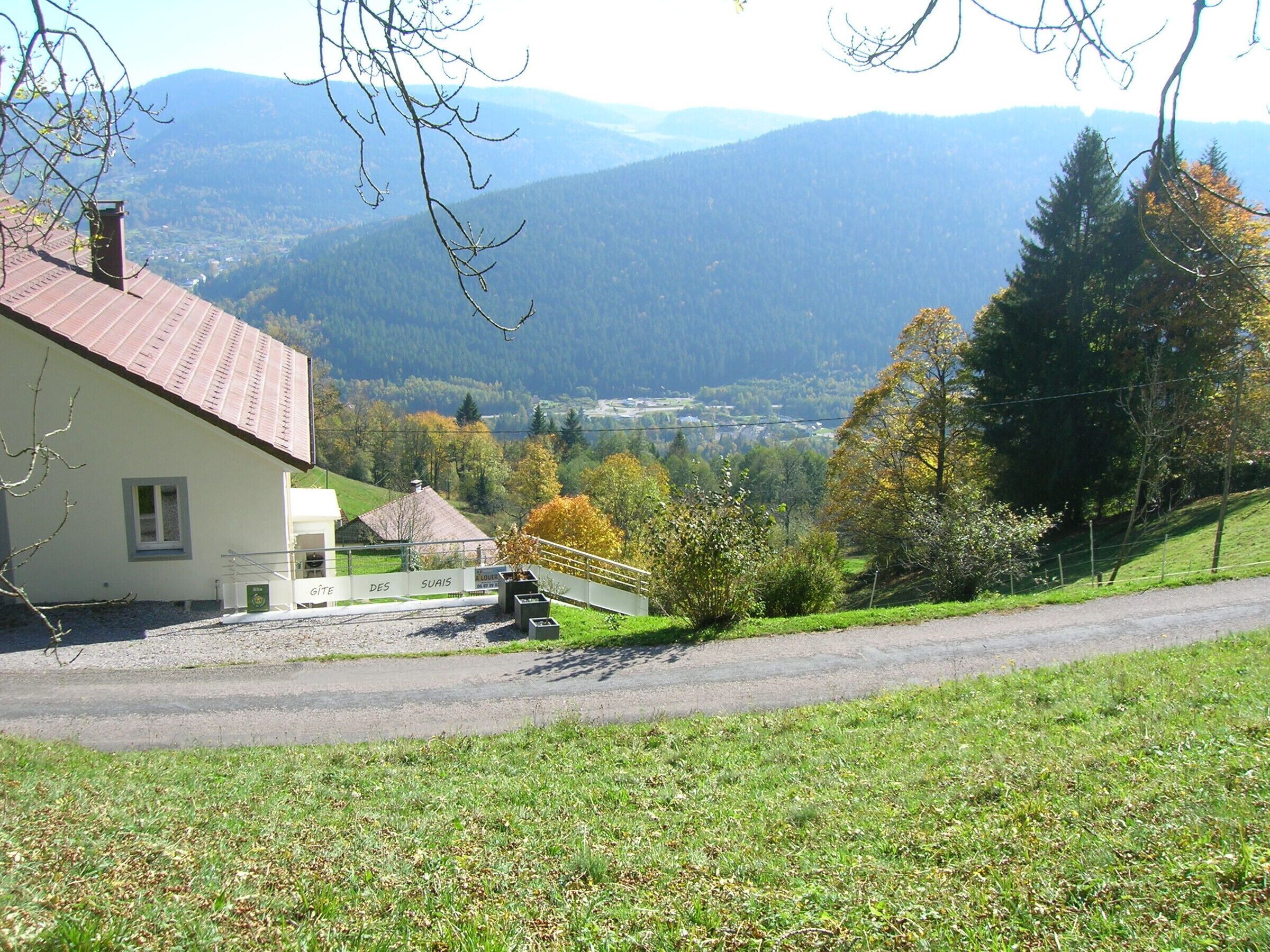 A rural house with a red roof, a gravel driveway, and a view of a valley with mountains in the background.