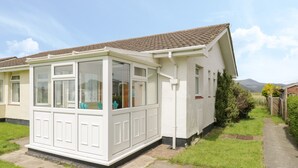 A single-story house with a conservatory, a tiled roof, and a pathway leading to the entrance. - Hafod-y-gors (Fairbourne)