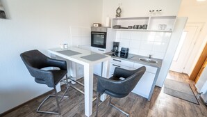 A modern kitchen with two black bar stools, a white countertop, and a built-in oven. - Ferienwohnung Anke - Appartement 5c (Heinsberg)