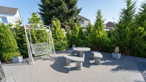 An outdoor patio area with a stone table and benches, surrounded by greenery and a metal gate. - Ferienwohnung Anke - Appartement 5c (Heinsberg)