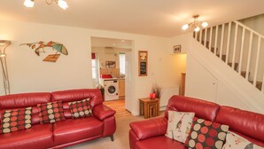 A living room with a red leather sofa, a small table, and a staircase. - White Goose Cottage (Whitby)