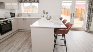 A modern kitchen with white cabinets, a central island with bar stools, a microwave, a kettle, and a window with a geometric valance.