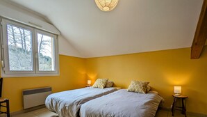 Un dormitorio con dos camas, una ventana que da a árboles, un radiador y una lámpara en el techo.