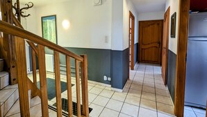 Un pasillo con una escalera de madera, una puerta y un refrigerador.