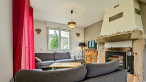 Un salón con un sofá gris, una mesa de centro de madera, una cortina roja, una chimenea y un televisor sobre un mueble.