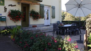 A building with a sign reading "Gite Les P'tites Bonnes Vignes" and a patio area with a table and chairs under a large umbrella.