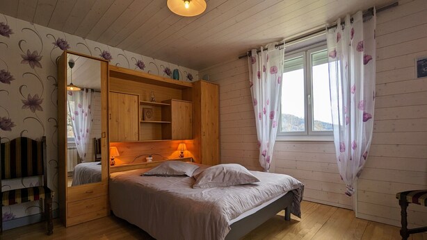 A bedroom with a wooden bed, a mirror, and a window with curtains.