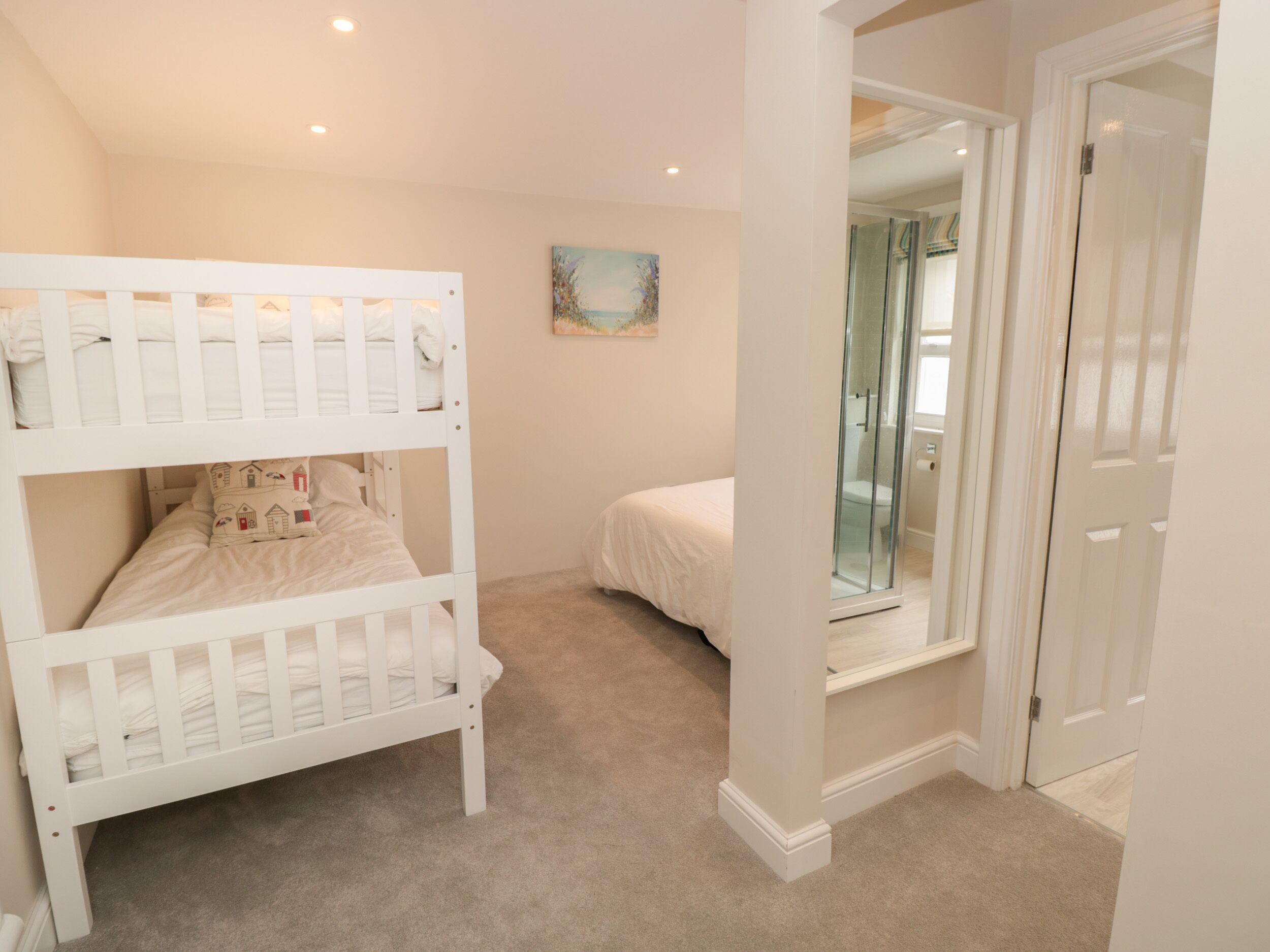 Un dormitorio con literas, una cama individual, ducha de vidrio y una puerta que da a otra habitación.
