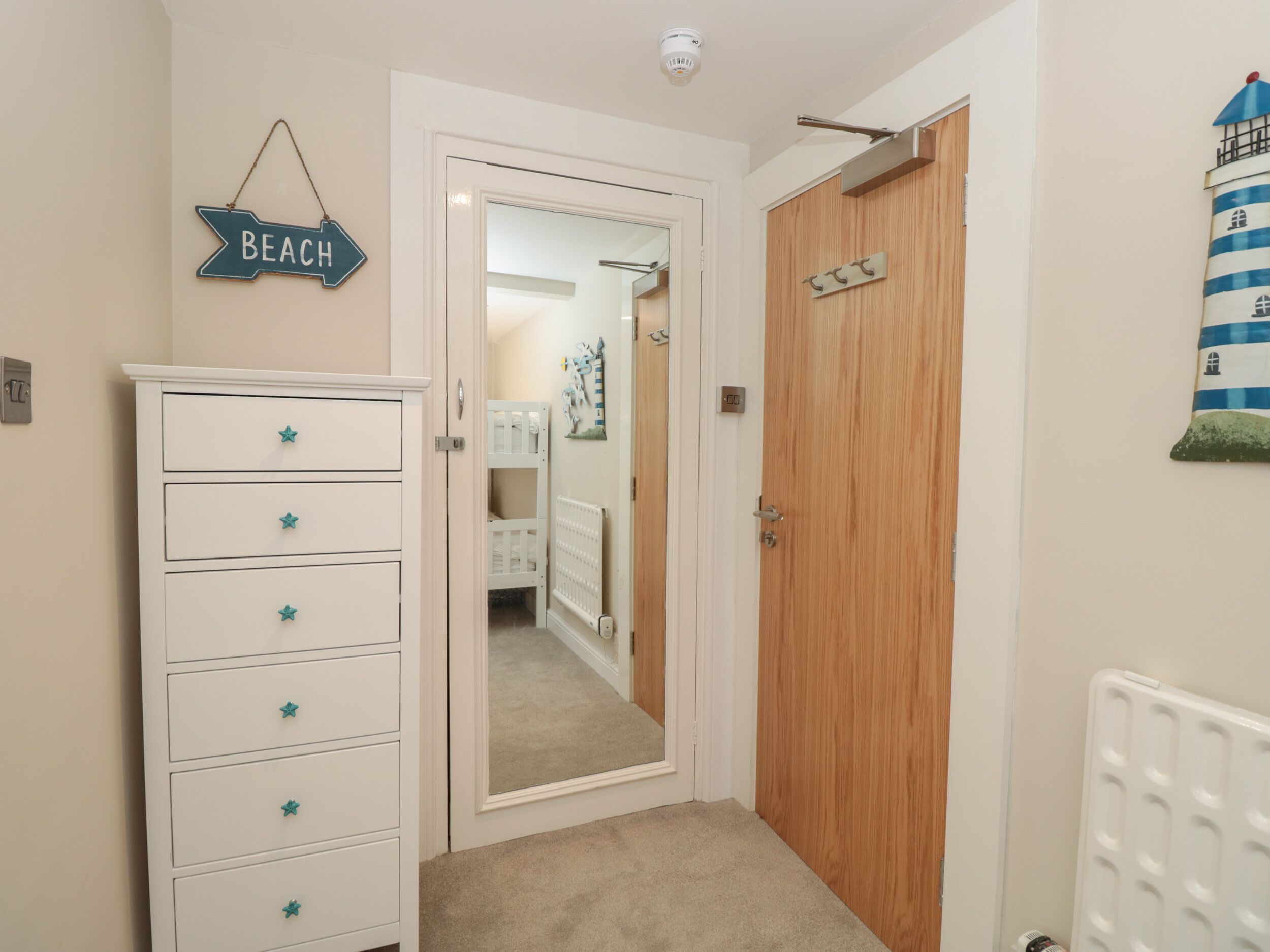 A hallway with a white dresser, a door leading to a bedroom, and a wall-mounted sign that says 'BEACH'.
