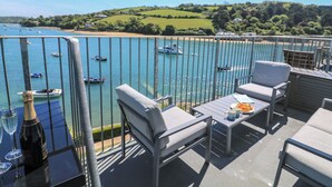 A balcony with outdoor furniture, a table with a bottle and glasses, and a view of boats on a body of water. - 37 The Salcombe (Salcombe)