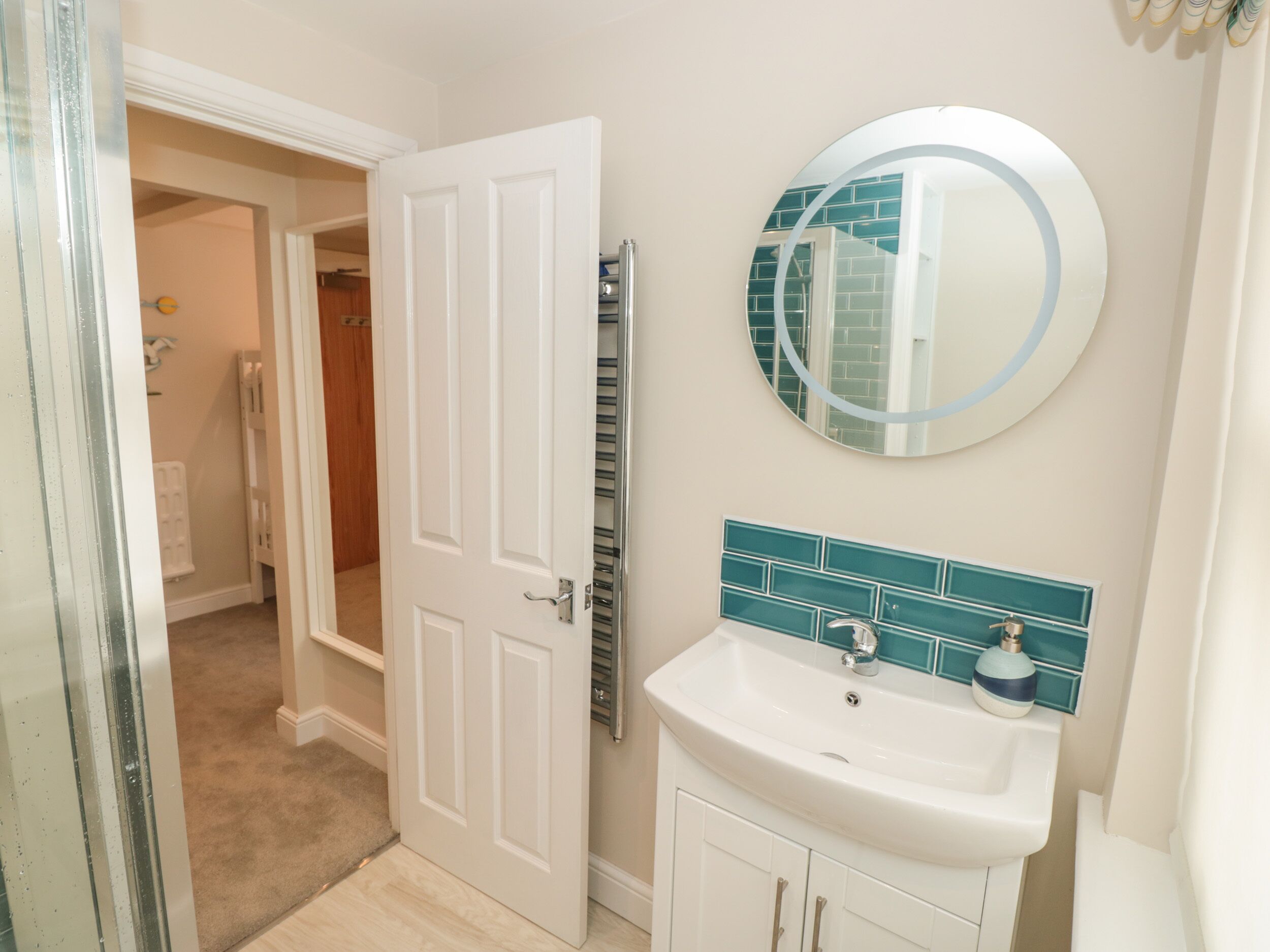 A bathroom with a white door, a white sink, and a mirror with a blue-tiled backsplash.