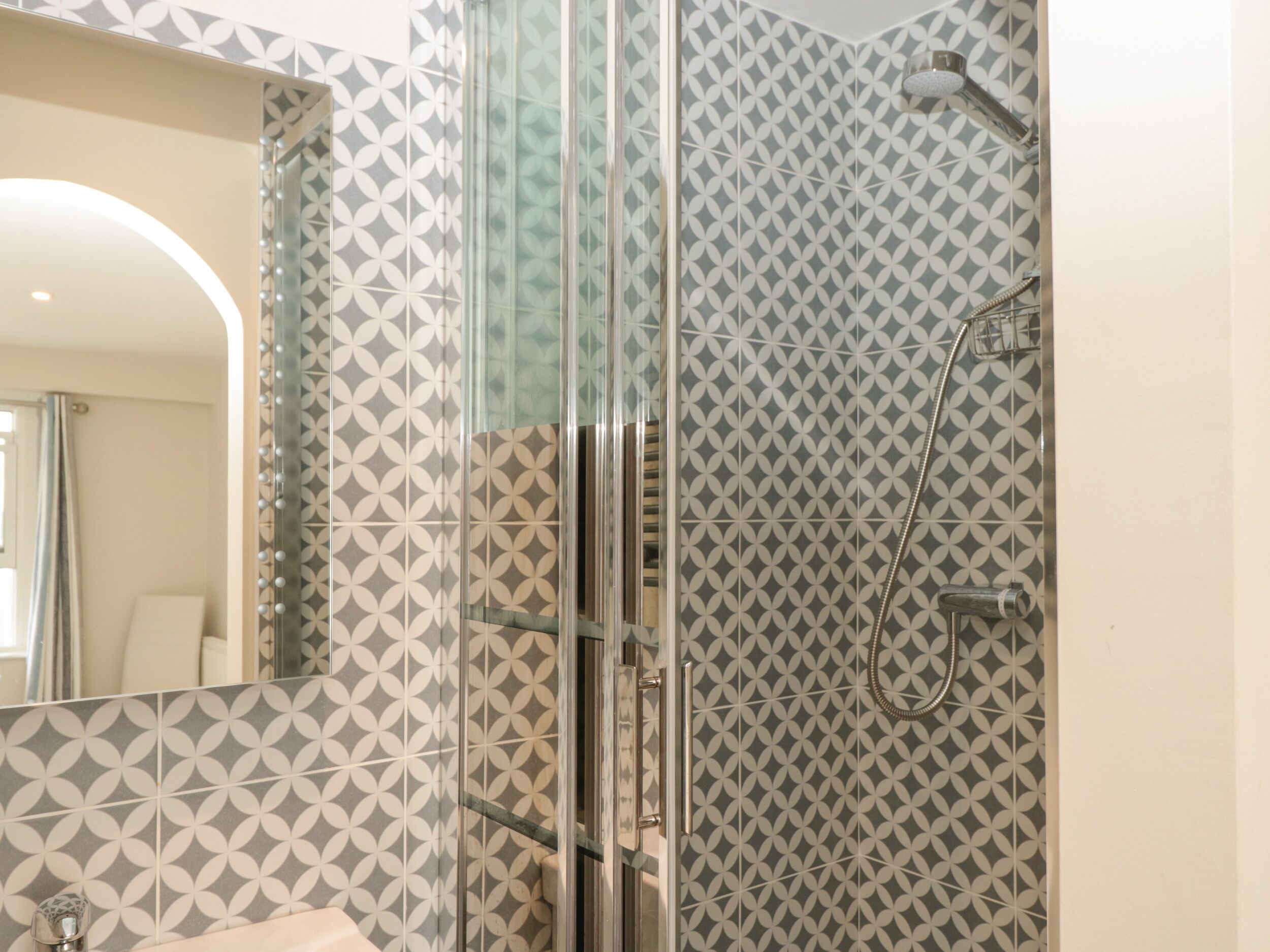 A modern bathroom with patterned tiles, a glass shower enclosure, and a visible sink area.