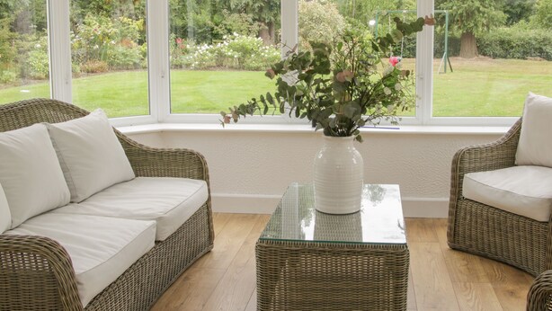 A room with wicker furniture, a glass coffee table, and a view of a garden through large windows. - The Big Dingle (Church Stretton)