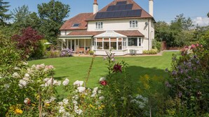 A two-story house with a conservatory, a garden with various flowers, and a solar panel on the roof. - The Big Dingle (Church Stretton)