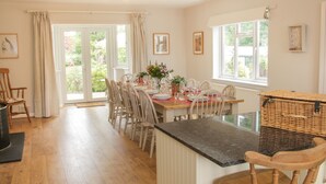 A dining area with a wooden table set for six, surrounded by chairs, a wicker basket, and a view of greenery outside. - The Big Dingle (Church Stretton)