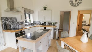 A modern kitchen with a central island, white cabinetry, and a black backsplash. - The Barn (Redditch)