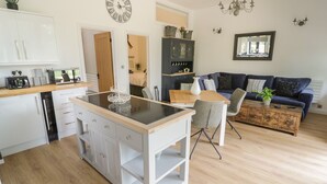 A modern kitchen with a central island, a dining area with a wooden table and chairs, and a living area with a sofa and a coffee table. - The Barn (Redditch)