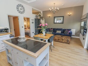 A modern kitchen with a central island, a dining area with a wooden table, and a living room with a blue sofa. - The Barn (Redditch)