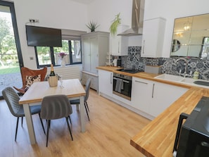 A modern kitchen with a dining area, wooden flooring, and a view of the outdoors. - The Leat (Redditch)