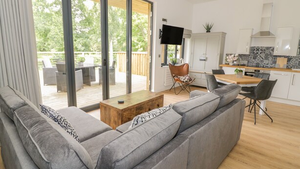 A modern living room with a grey sofa, a wooden coffee table, and a dining area with a wooden table and chairs. - The Leat (Redditch)