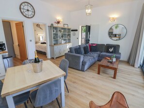 A modern living room with a sofa, a dining table with chairs, a coffee table, and a kitchen area with a microwave. - The Leat (Redditch)