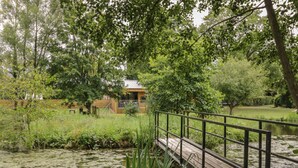 A wooden bridge over a pond with a building in the background. - The Leat (Redditch)