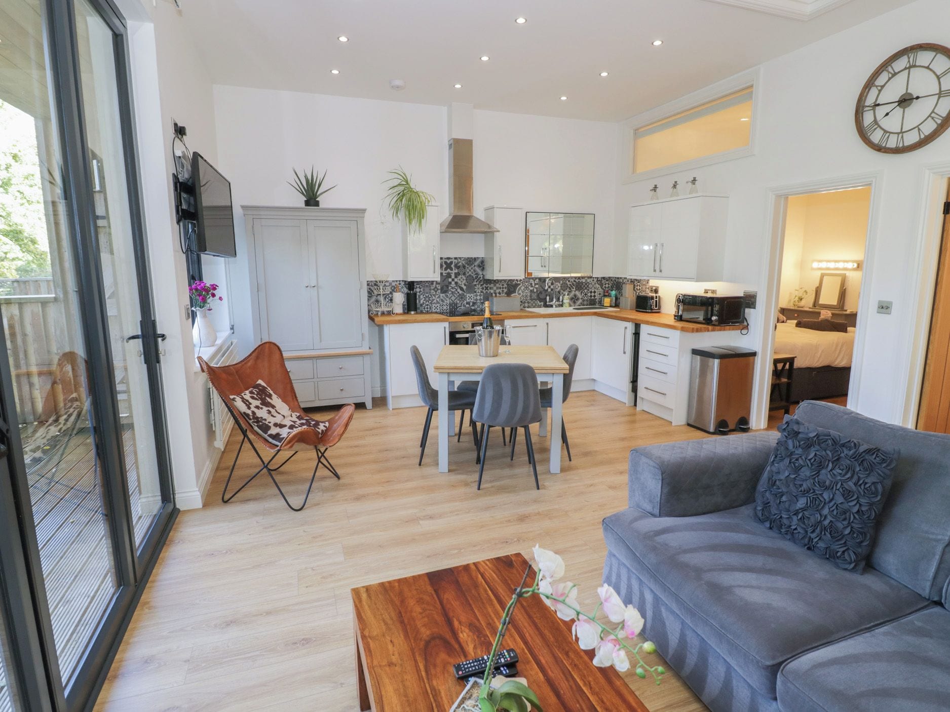 A modern living room with a grey sofa, a wooden coffee table, and a dining area with a table and chairs.