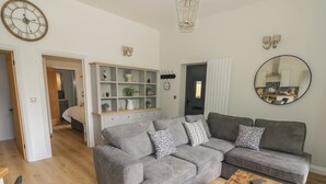 A modern living room with a grey sectional sofa, a wooden coffee table, and a white shelving unit with decorative items. - The Leat (Redditch)