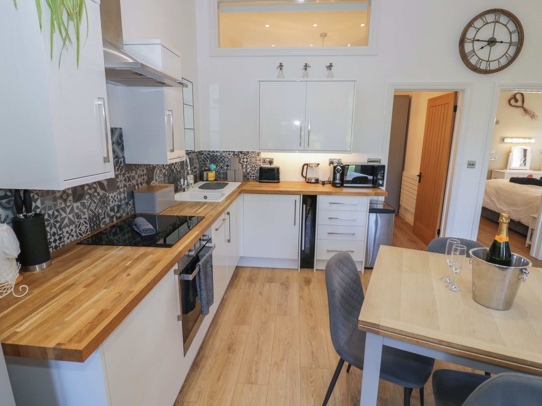 Una cocina compacta con armarios blancos, encimera de madera, microondas, cafetera y lavamanos.