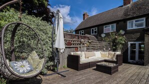 Une terrasse en bois avec des meubles d’extérieur, un fauteuil suspendu et un espace jardin agrémenté d’une clôture et de plantes.