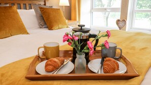 A neatly made breakfast tray with croissants, a coffee pot, and a vase of flowers on a bed with a wooden headboard and pillows. - Shep Cottage (Hebden Bridge)