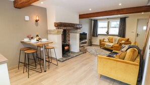 A modern living room with a yellow sofa, a fireplace, and a dining area with stools. - Shep Cottage (Hebden Bridge)