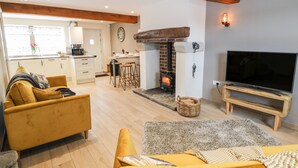A living room with a sofa, TV, fireplace, kitchen in the background, and a dining area. - Shep Cottage (Hebden Bridge)