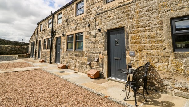 A stone building with multiple doors and windows, a gravel driveway, and a metal chair outside. - Shep Cottage (Hebden Bridge)