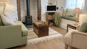 A cozy living room with a stone wall, a fireplace, a television, and a comfortable seating area. - Clover Cottage (Plymouth)