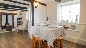 A dining area with a table set for two, a wooden chair, a small cabinet, and a window with plants. - Clover Cottage (Plymouth)