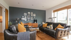 A modern living room with leather sofas, a wooden sideboard, and a large window with a telescope. - The Bolt Hole (Torpoint)