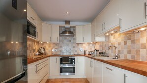 A modern kitchen with wooden countertops, stainless steel appliances, and a tiled backsplash. - The Bolt Hole (Torpoint)