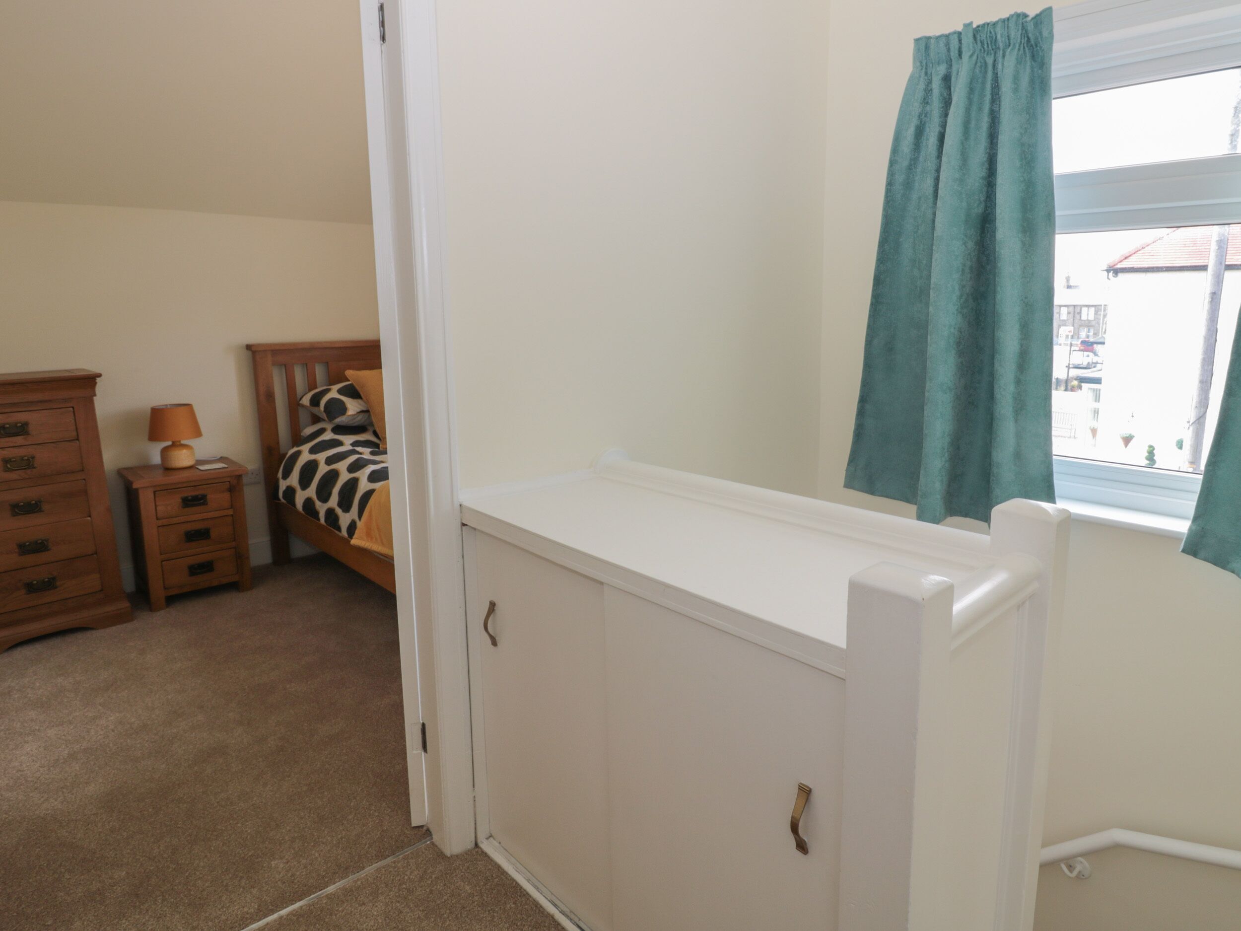 Un dormitorio con cama, cómoda, radiador y ventana con cortinas.