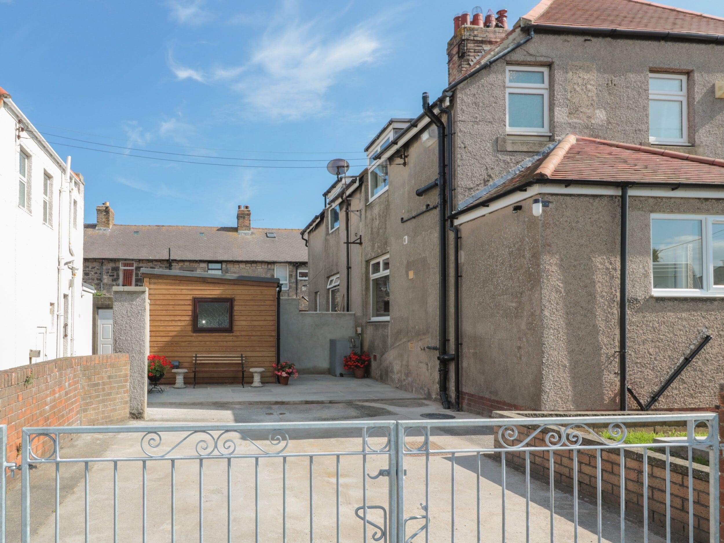 Une rue résidentielle bordée de maisons, avec une entrée fermée par un portail et une petite construction en bois.