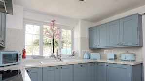 Una cocina con armarios azules, horno empotrado, lavabo y ventana con vistas al verdor.