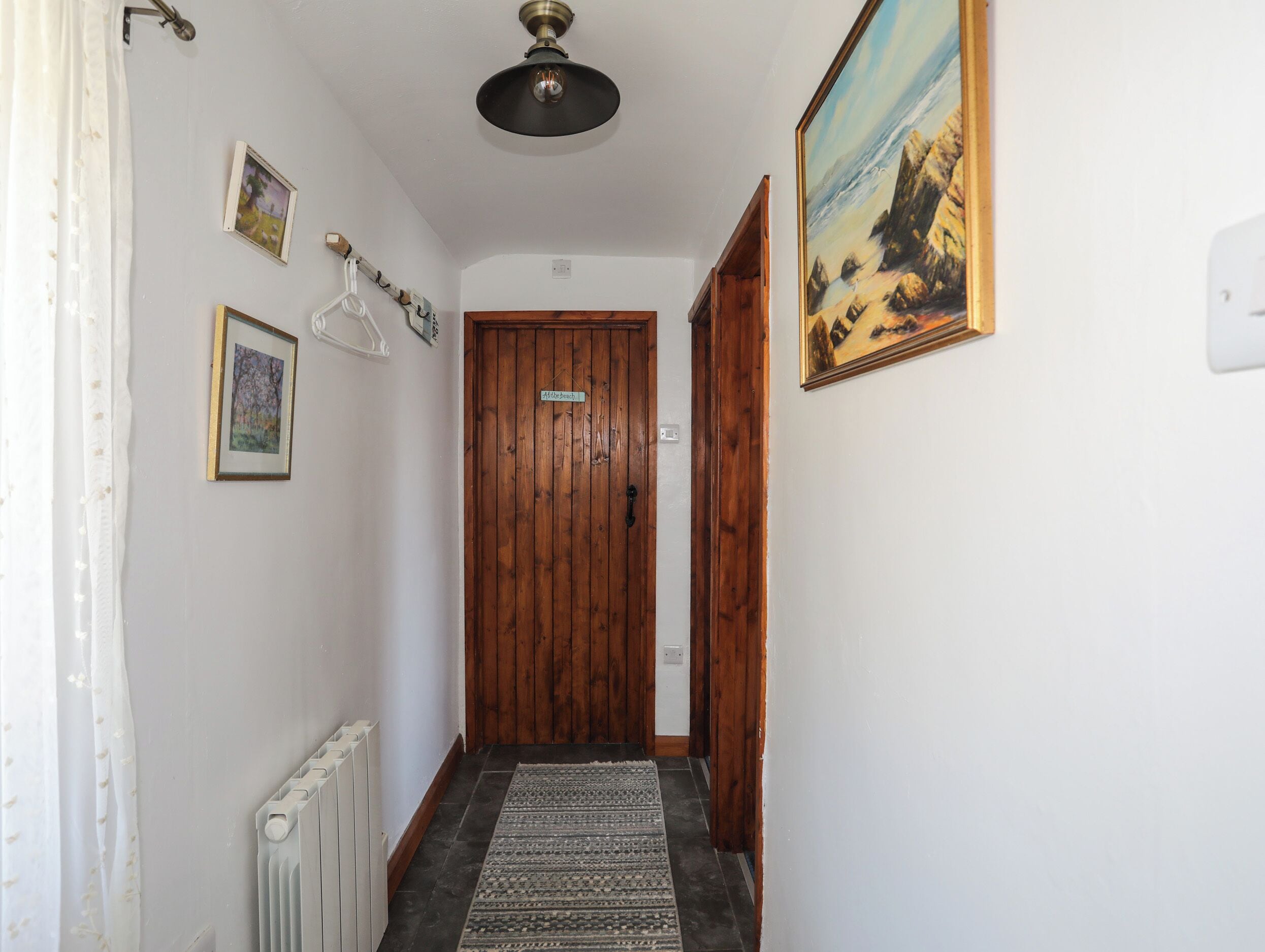 A hallway with a wooden door, a radiator, a patterned rug, and a painting on the wall.
