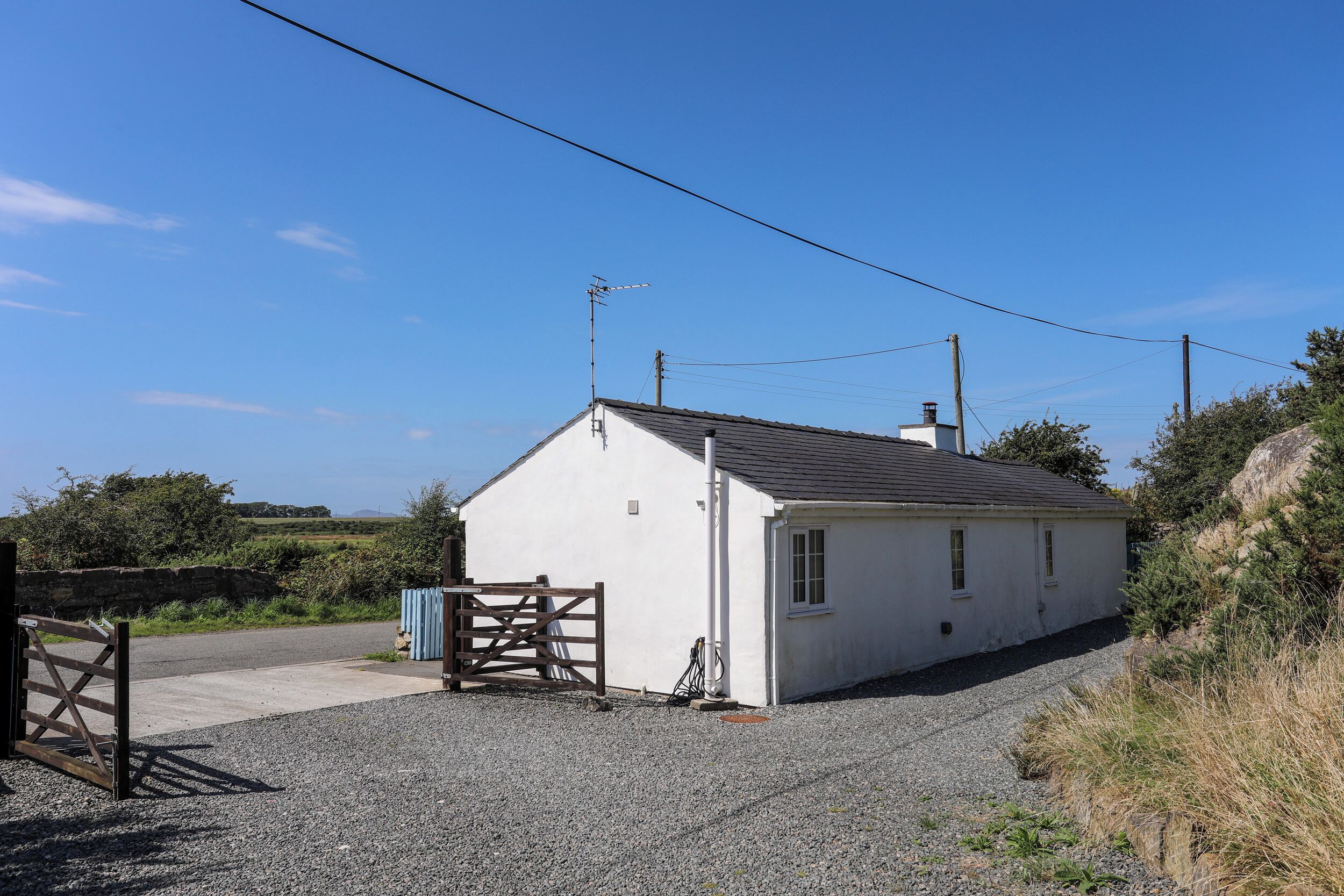 A small white building with a gravel driveway and a wooden gate.
