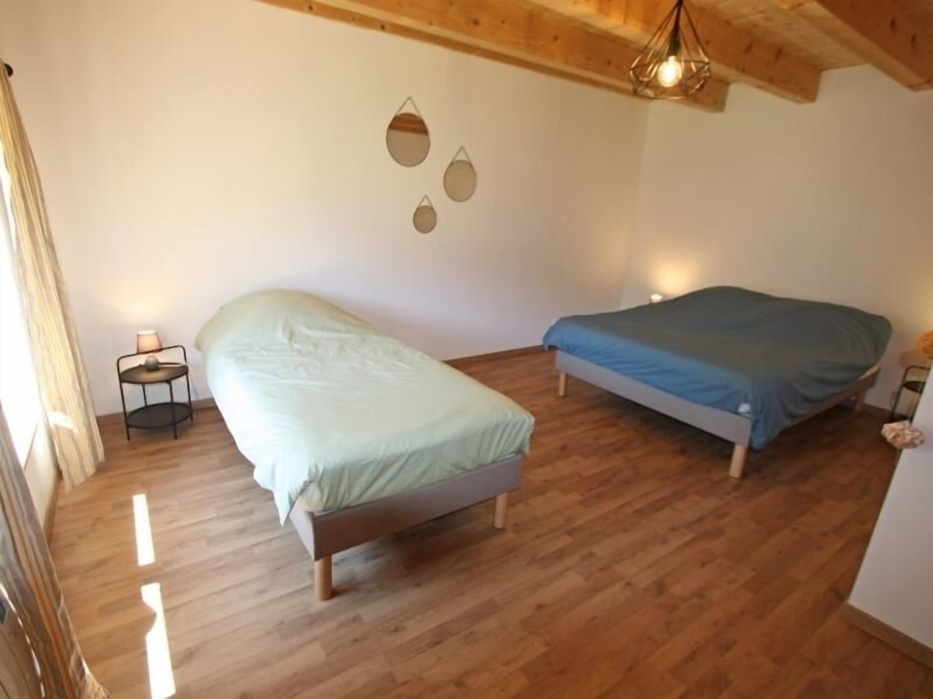 Una camera da letto con due letti, pavimento in legno e soffitto spiovente con lampadario.
