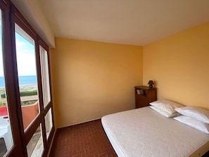 A room with a bed, a nightstand, a window with a view, and a door.