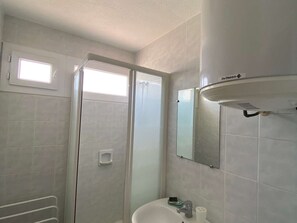 A bathroom with a shower, a sink, a mirror, and a window.