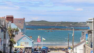 A coastal street with parked cars, a surf shop, and a view of the sea.