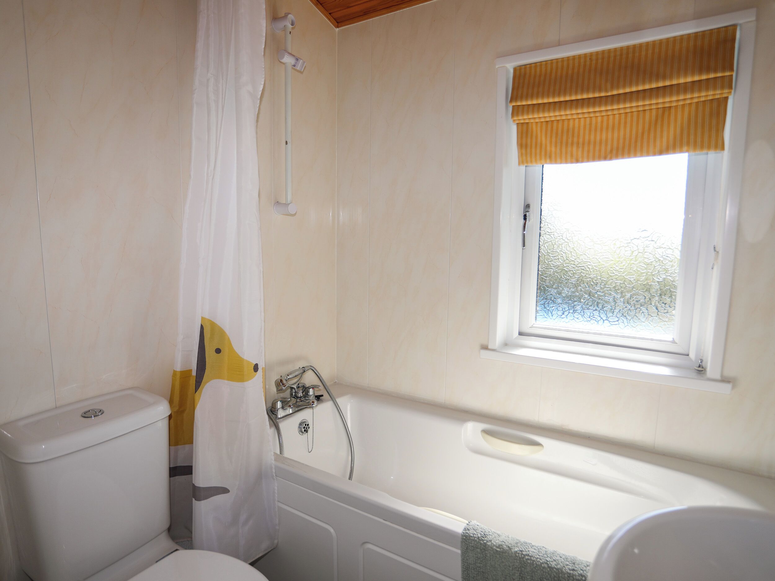 Une salle de bain comprenant des toilettes, une douche avec un rideau, une baignoire et une fenêtre avec un store jaune.